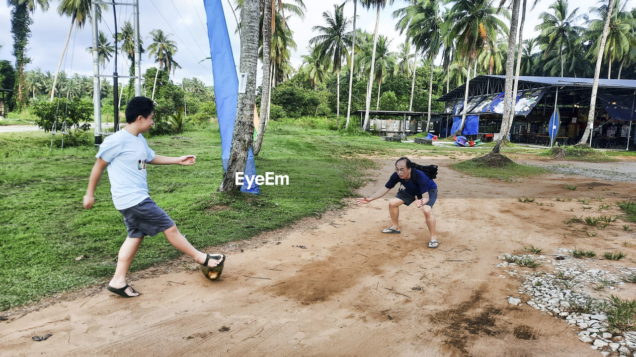 Father and son having fun playing soccer with a coconut in the playground.