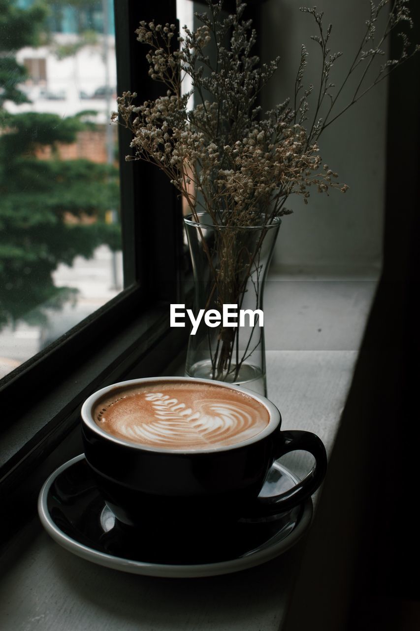Close-up of coffee by flower vase on window sill