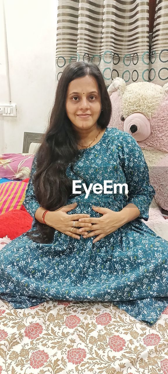 one person, women, looking at camera, portrait, sitting, adult, smiling, front view, lifestyles, indoors, furniture, happiness, hairstyle, long hair, young adult, pattern, clothing, relaxation, home interior, leisure activity, casual clothing, textile, full length, black hair, female, dress, art, brown hair, emotion, three quarter length, domestic room, carpet