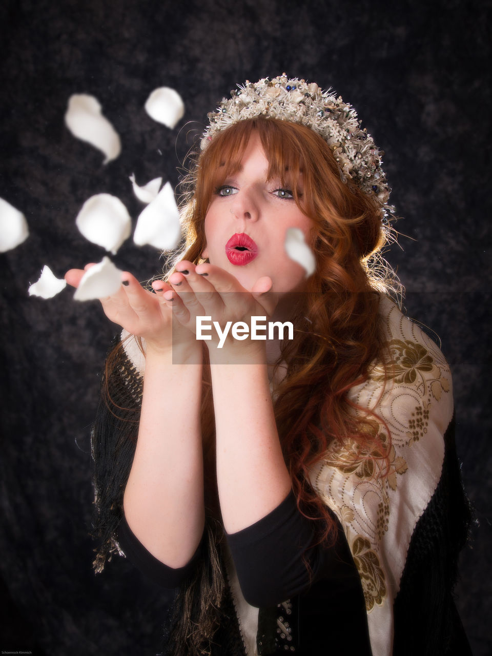 Woman blowing white petals against black background