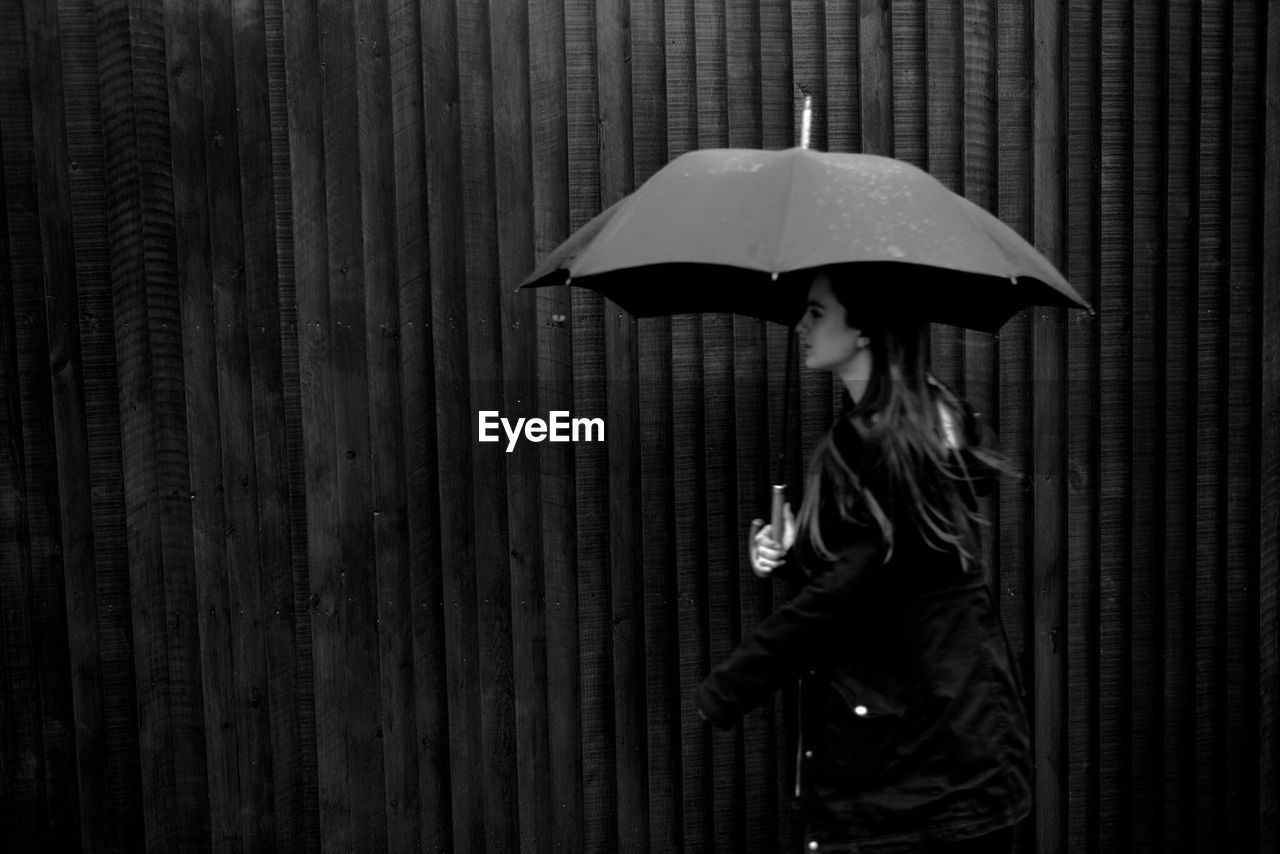 Side view of woman with umbrella walking by wall