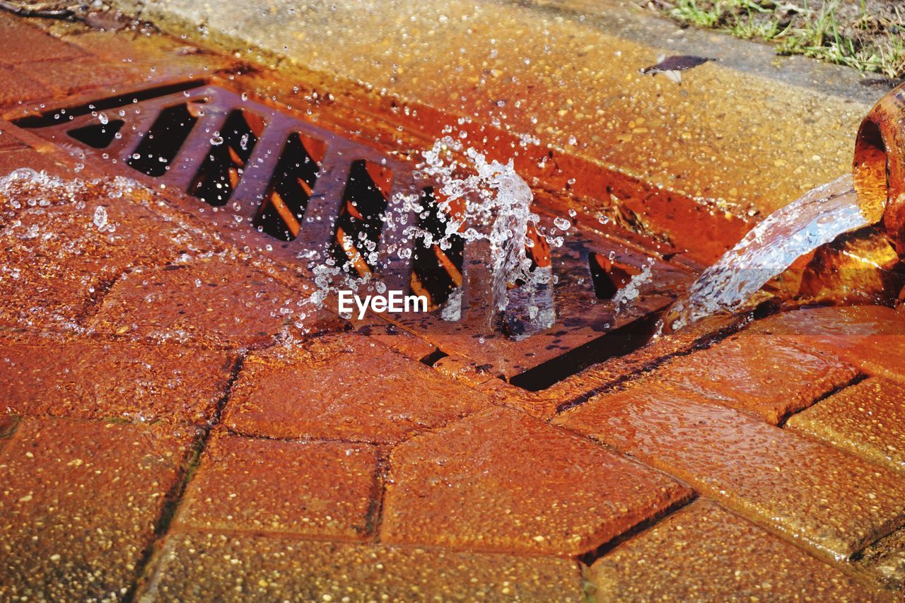 Water flowing from pipe over drain on footpath