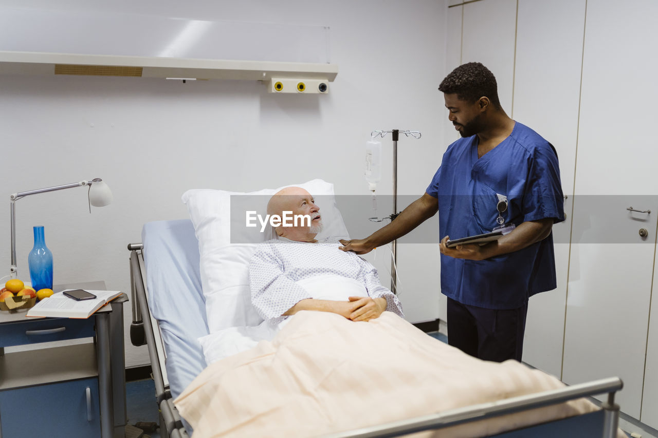 Male nurse with hand on shoulder of senior patient lying in hospital