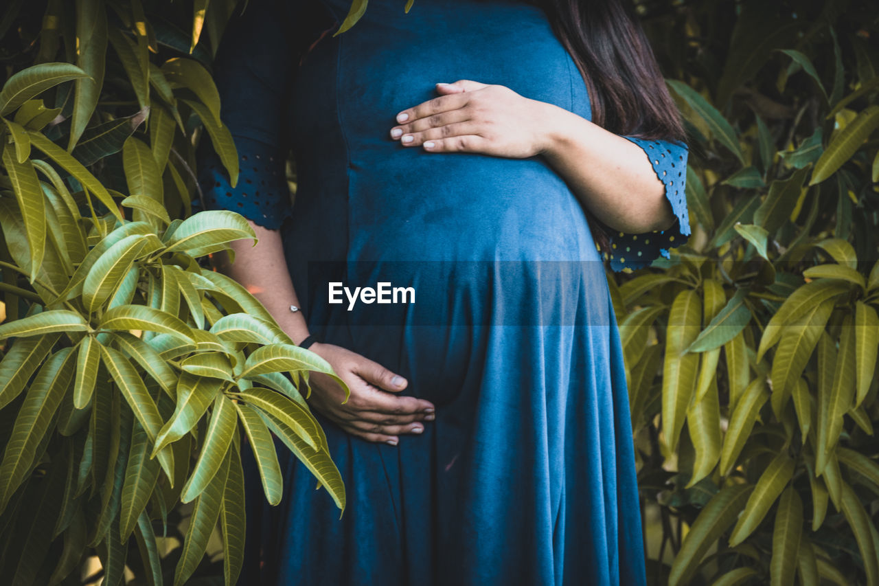 Midsection of pregnant woman standing against plants