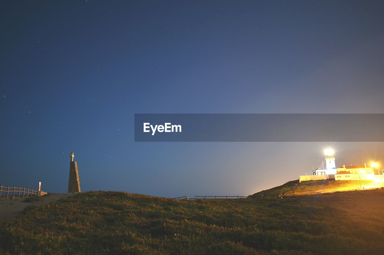 Lighthouse on field against clear sky at night