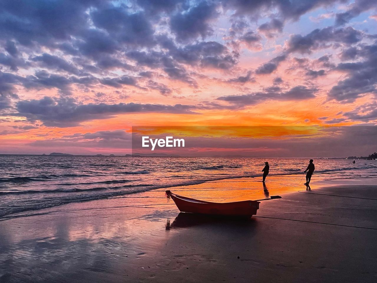 Scenic view of sea against twilight sky during sunset with silhouette of a boat  and two people.