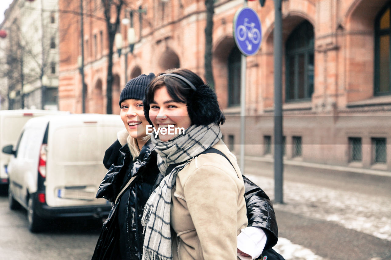 Portrait of cheerful young women wearing warm clothing while standing on street in city during winter