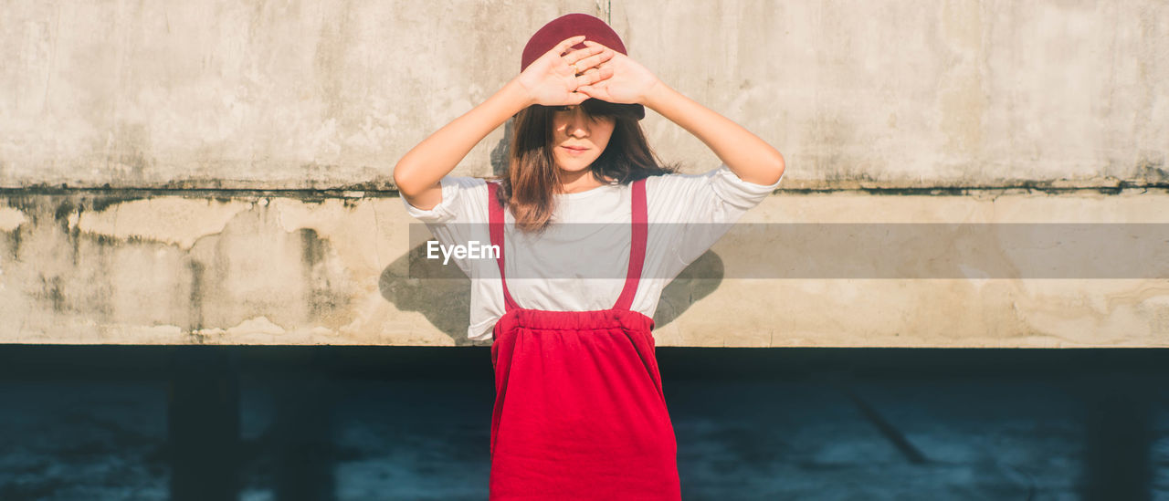 Young woman shielding eyes while standing against wall