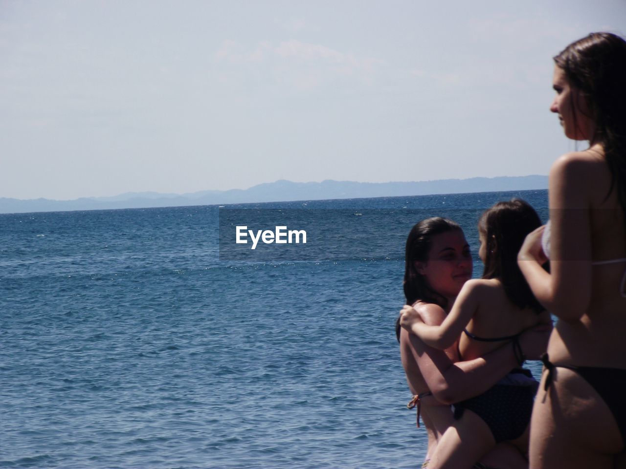 Mother carrying daughter by friend at beach during summer