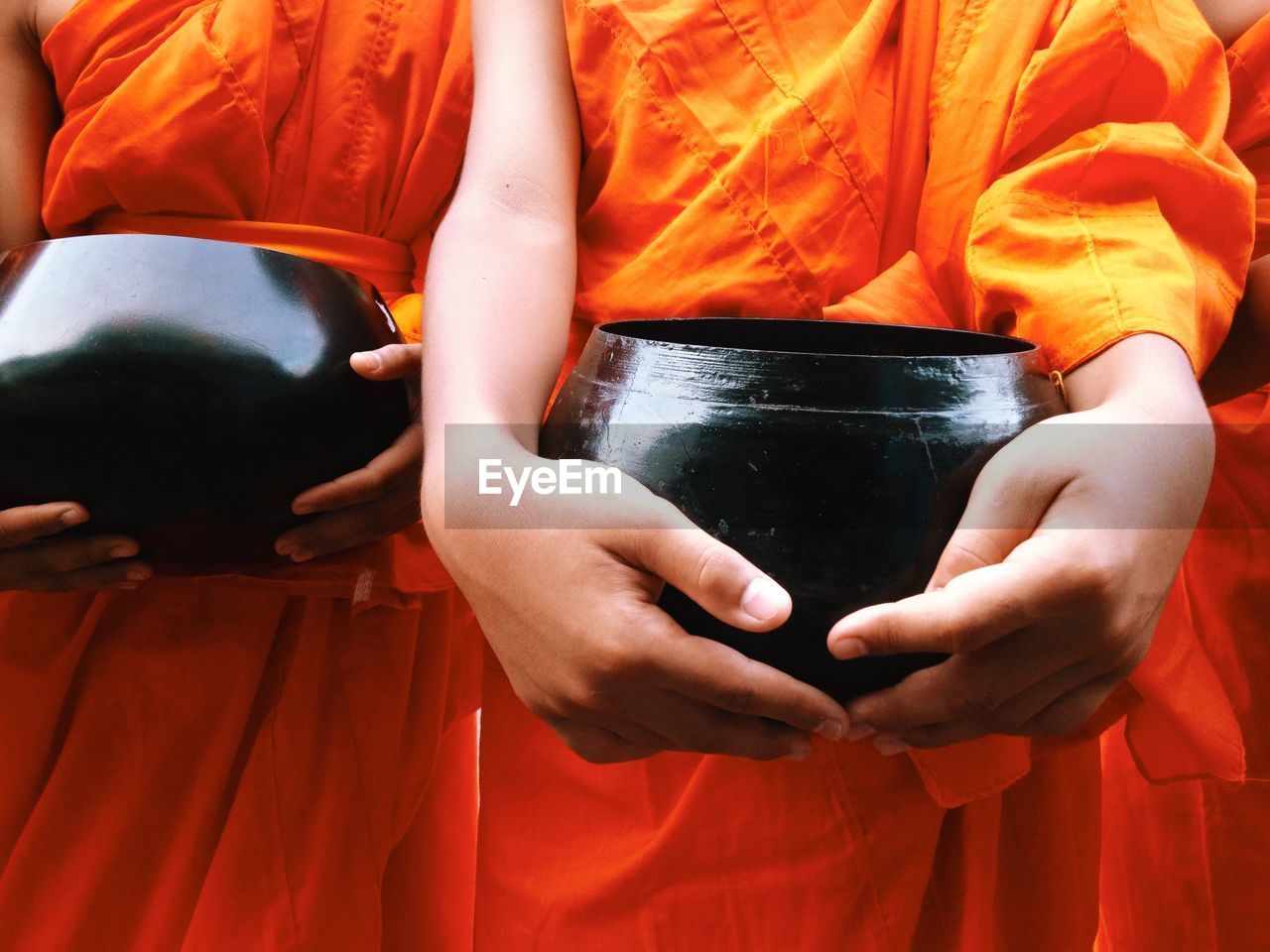 Midsection of monks holding container while standing in shrine