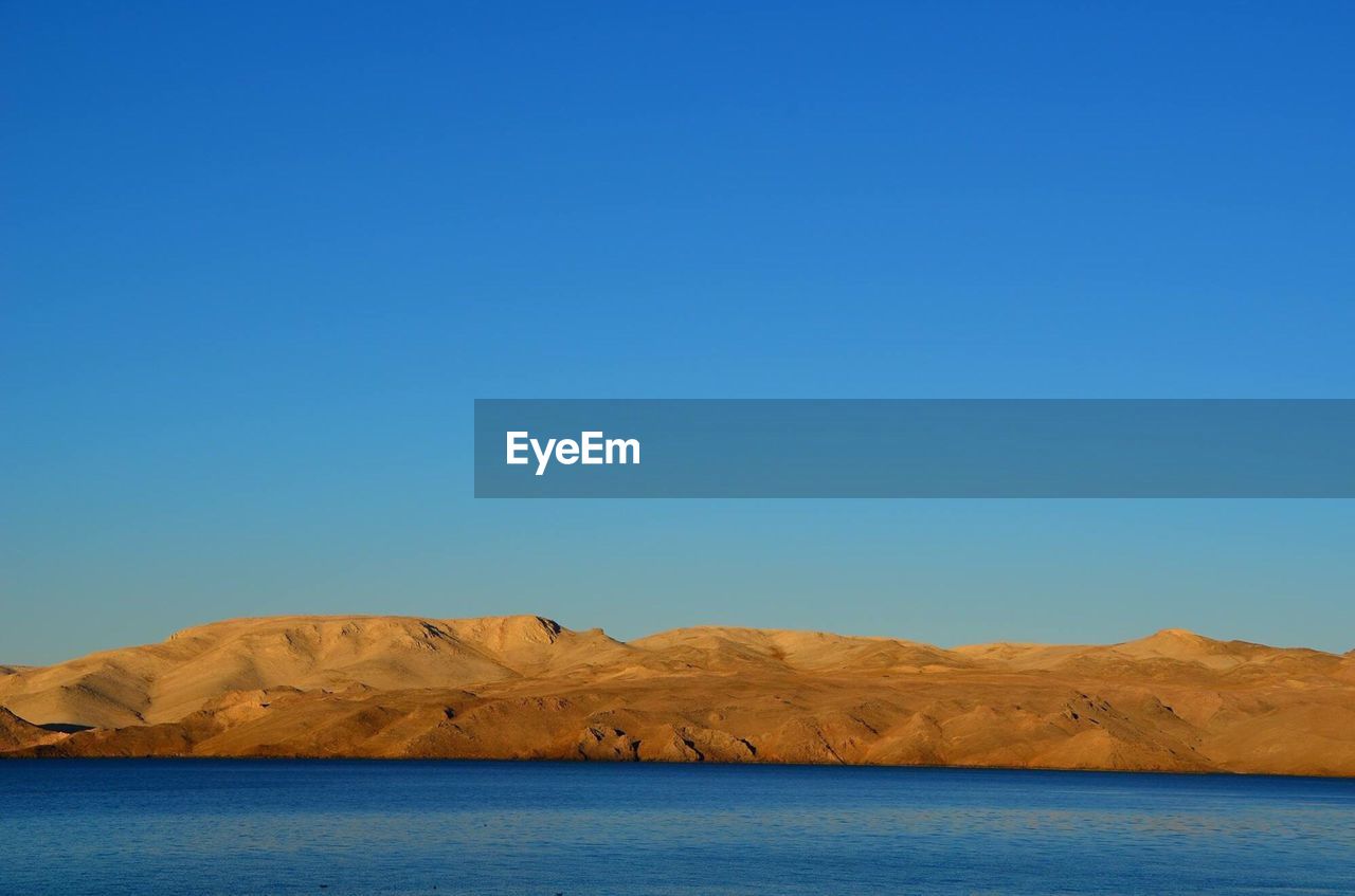 Scenic view of sea and sand dune against clear blue sky