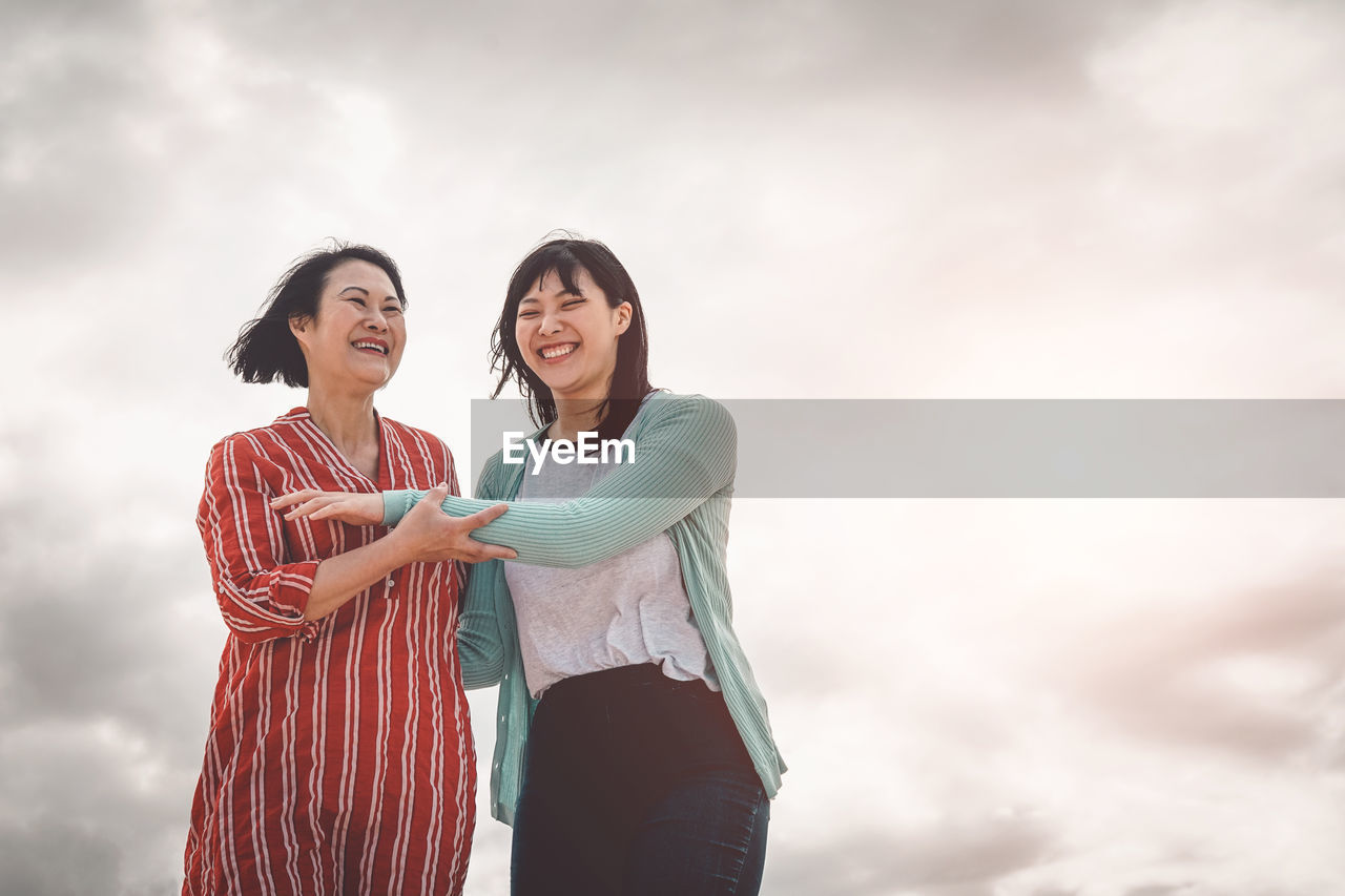 Happy mother and daughter standing against sky