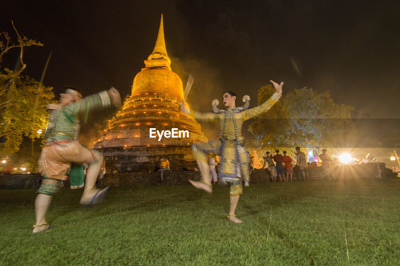 GROUP OF PEOPLE ENJOYING AT ILLUMINATED TEMPLE