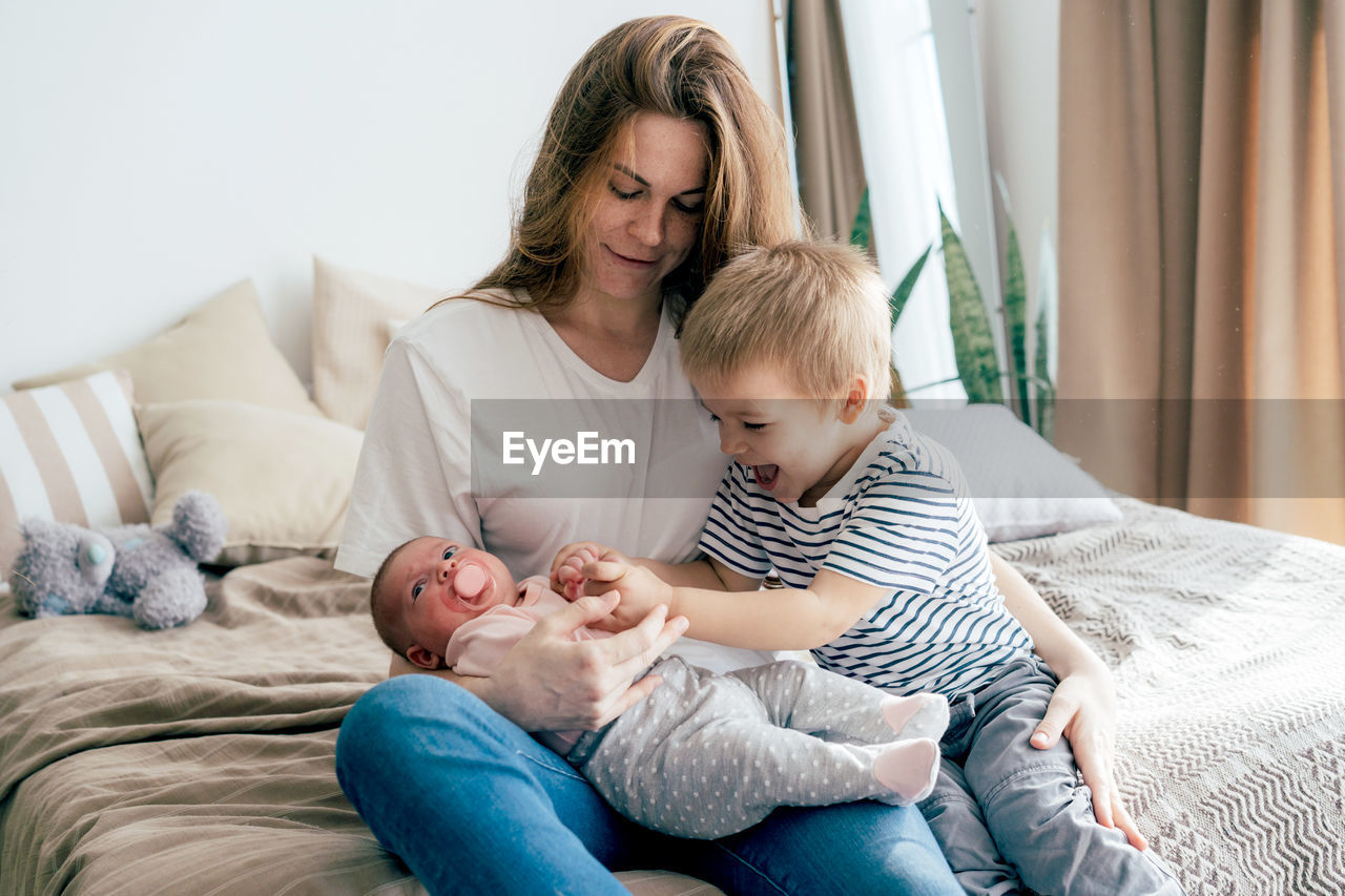 Young mother with children at home. newborn sister and brother toddler with parent.