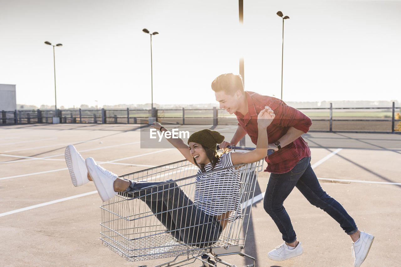 Playful young couple with shopping cart on parking level