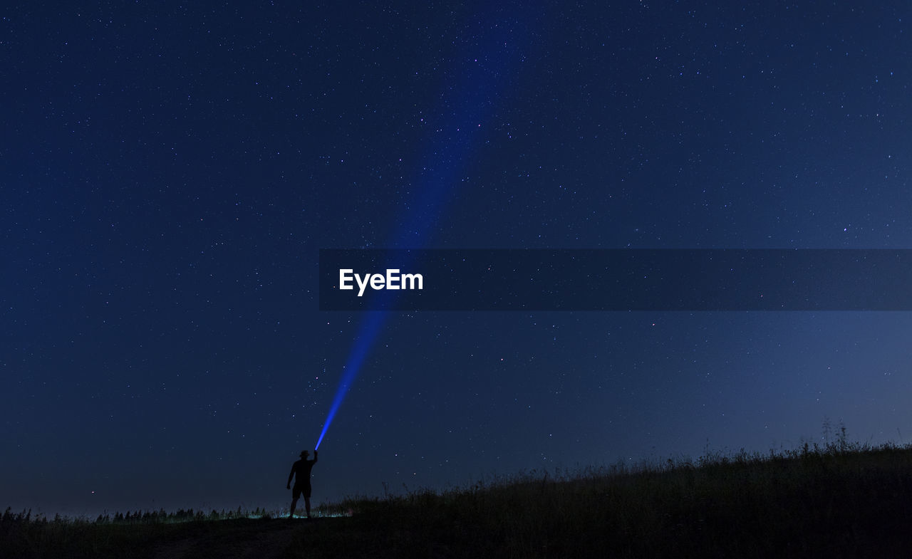 Silhouette man projecting flashlight in sky at night