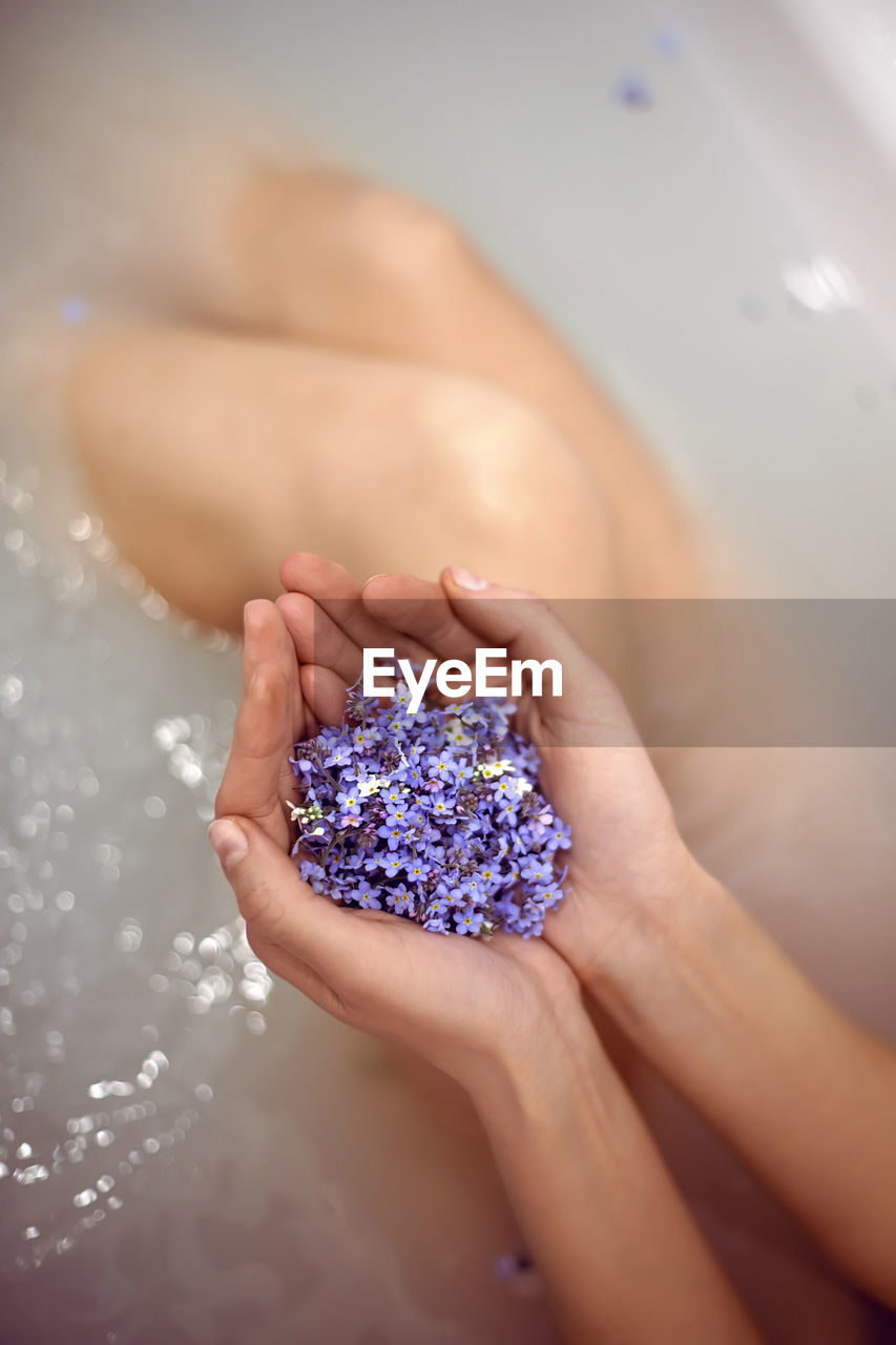 Woman is lying in the bath with water in the spa and holds small blue forget-me-nots in her hands