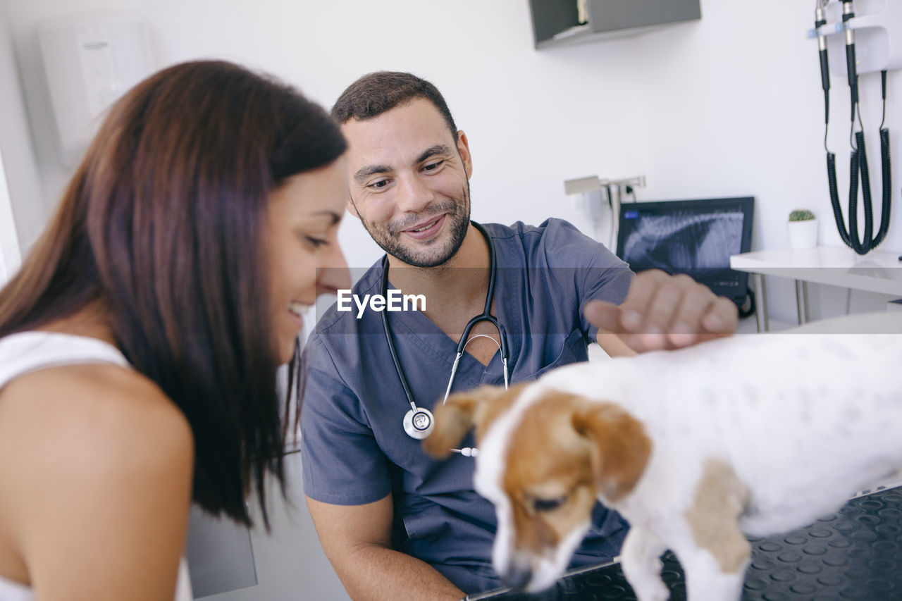 Woman and veterinarian playing with puppy in hospital