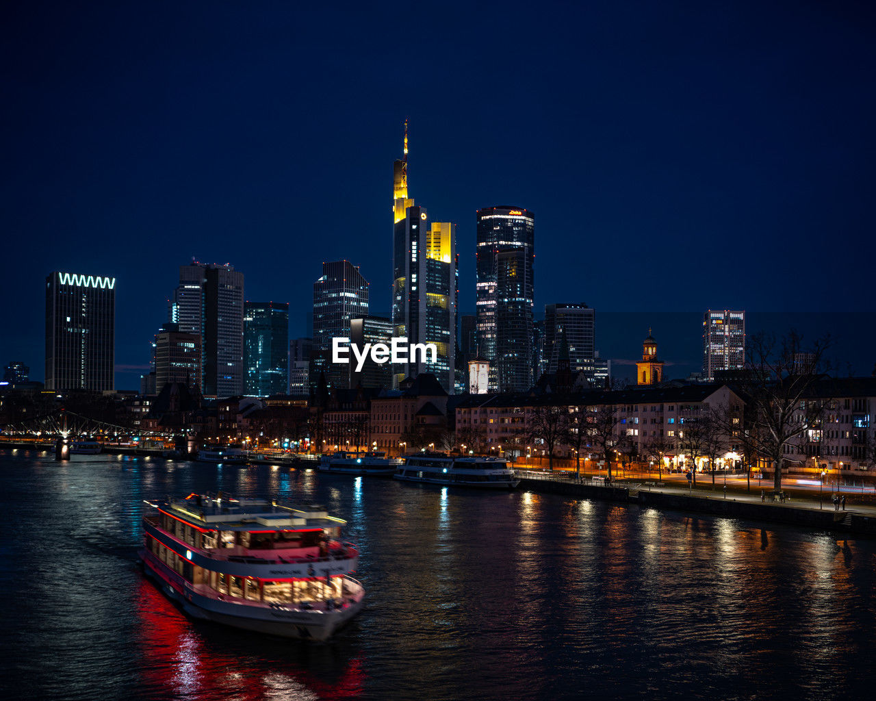 Illuminated buildings by river against sky at night