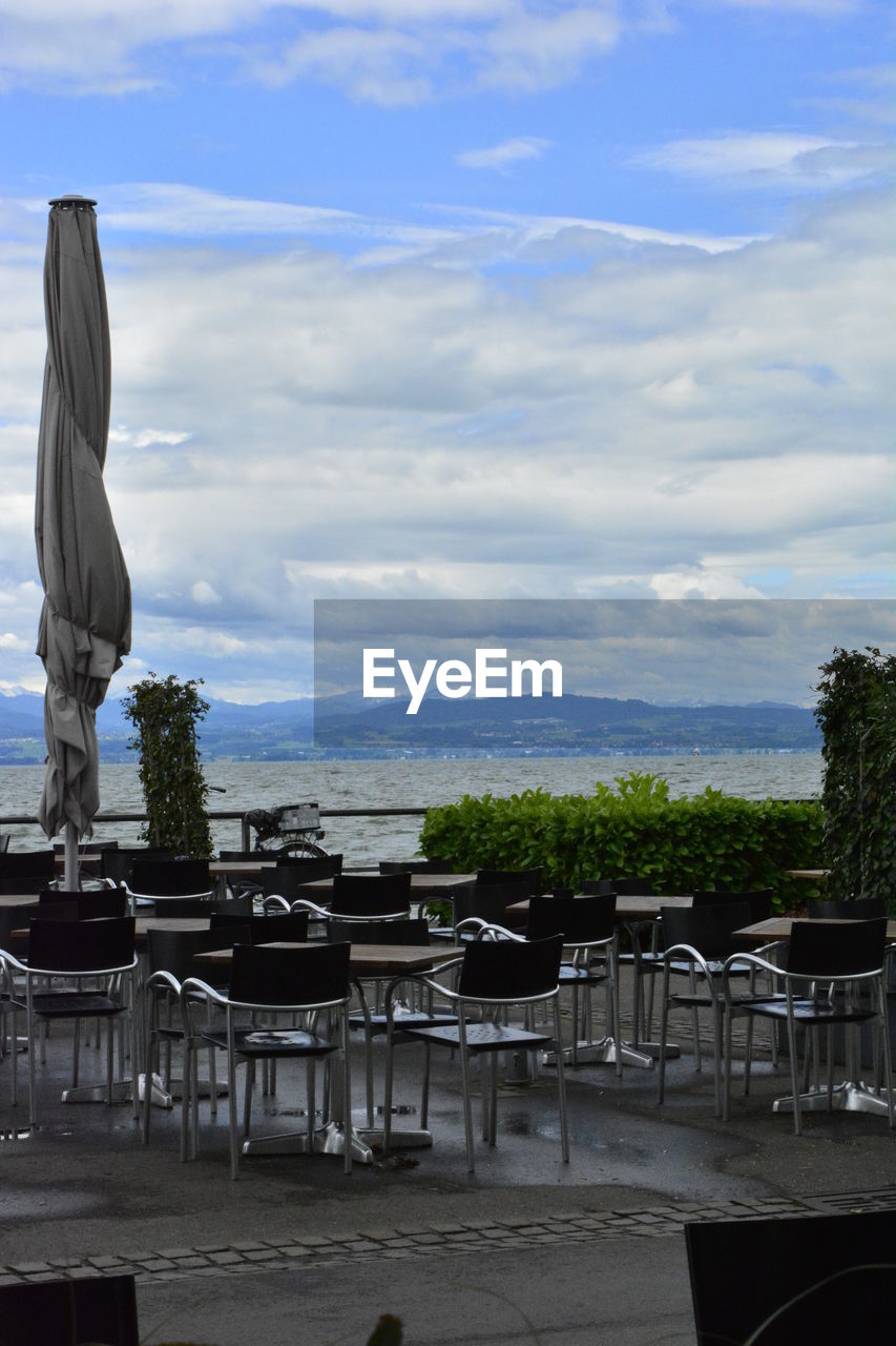 EMPTY CHAIRS AND TABLE AT RESTAURANT AGAINST SKY