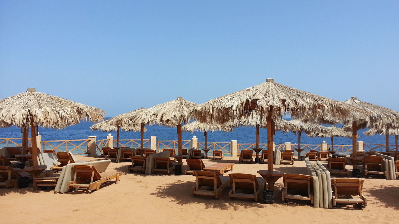 Lounge chairs on beach against clear blue sky