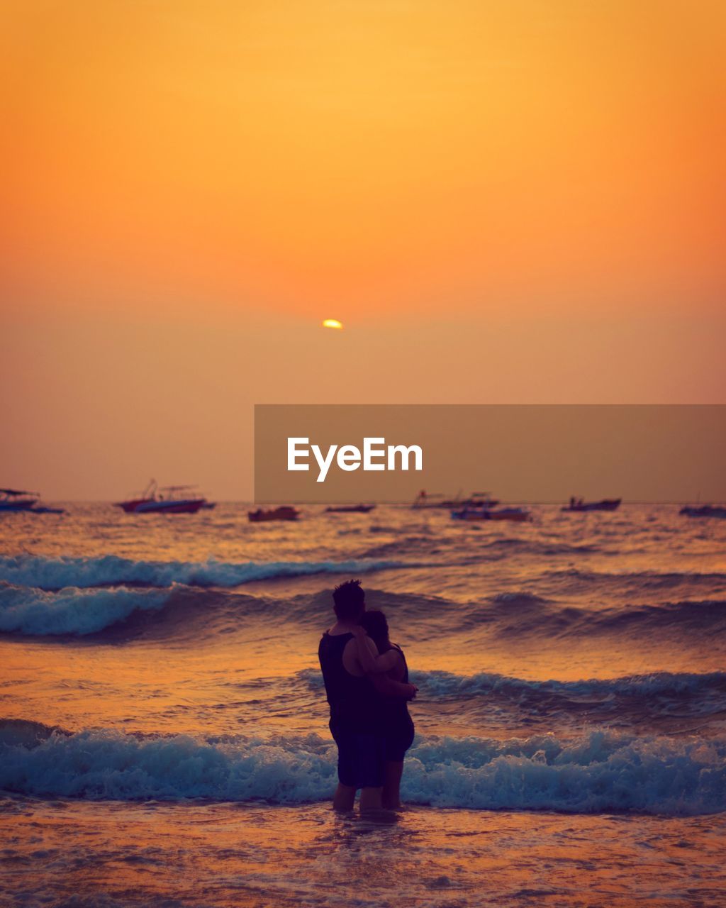 Couple standing on beach against sky during sunset