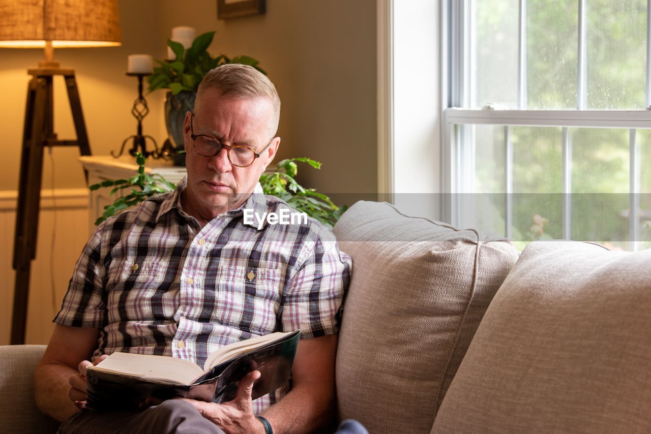 MIDSECTION OF MAN READING BOOK AT HOME