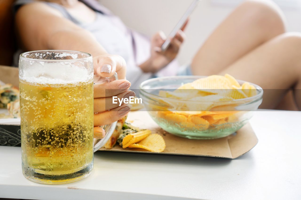 Woman hand holding glass of beer with potato chips, pizza on desk
