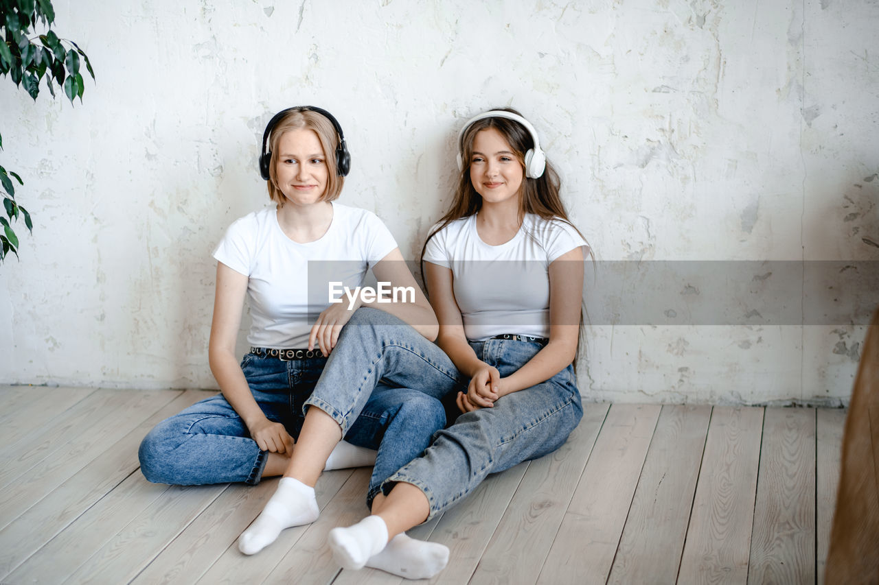Two teenage girls stand near a white wall in funny sunglasses. . headphones hang on their necks
