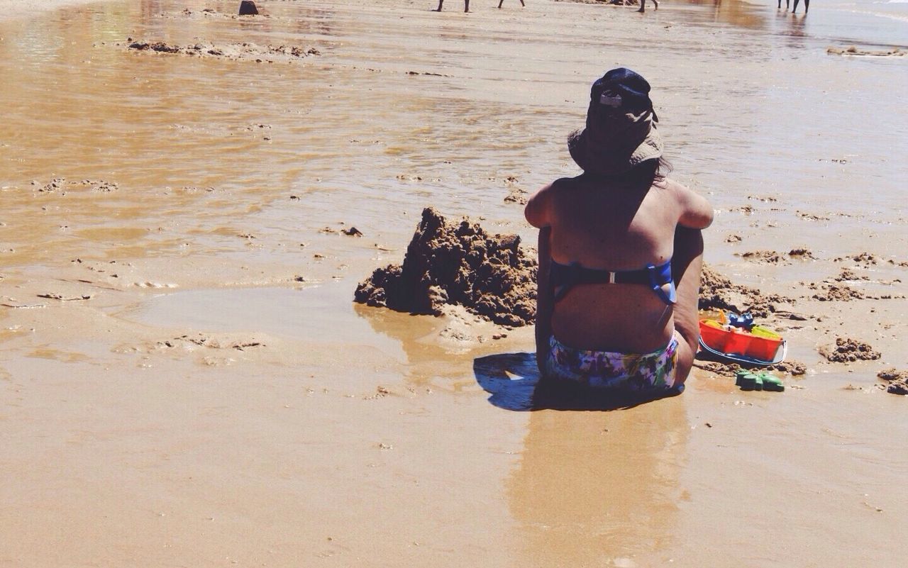 Rear view of woman sitting on wet shore