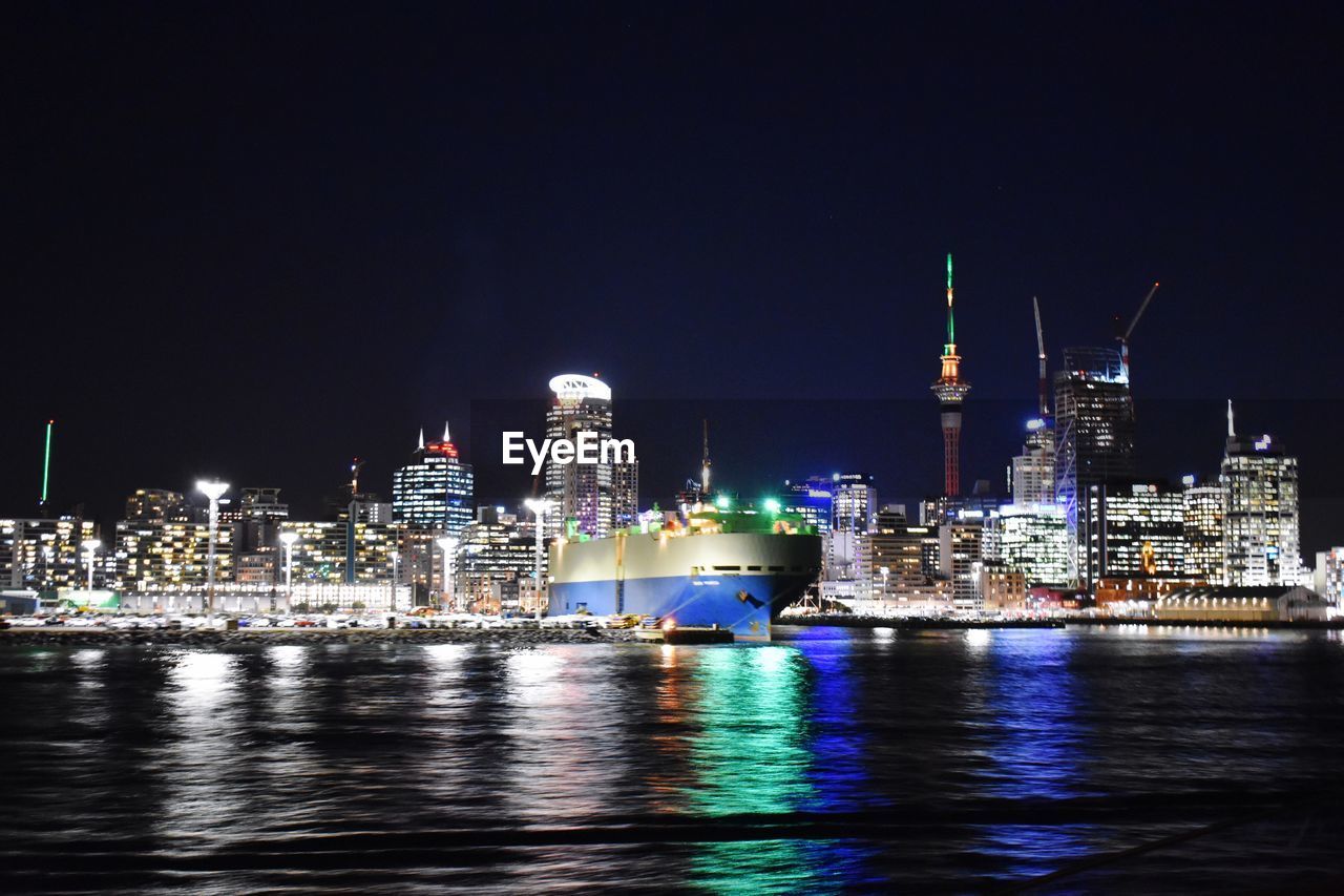 Illuminated cruise ship against modern buildings in city against sky at night