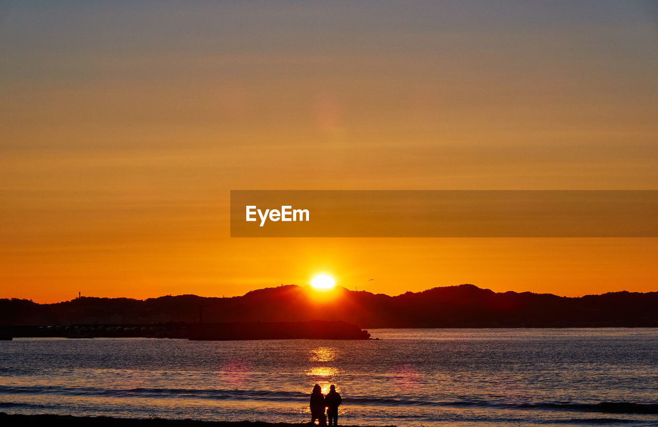 Silhouette people on beach against sky during sunrise