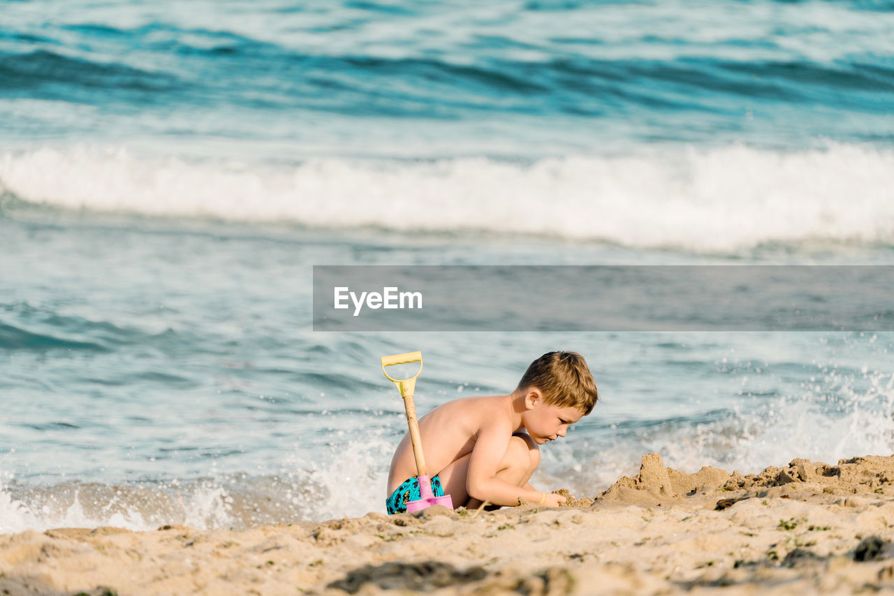 REAR VIEW OF SHIRTLESS BOY AT BEACH