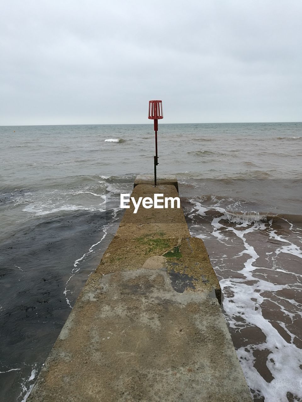 Pole on pier in sea against cloudy sky