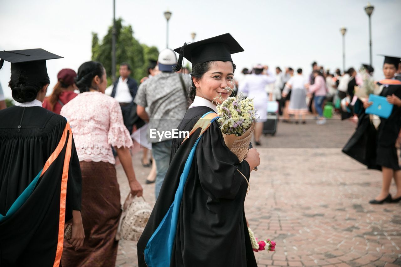 Smiling woman in graduation gown walking with crowd on street