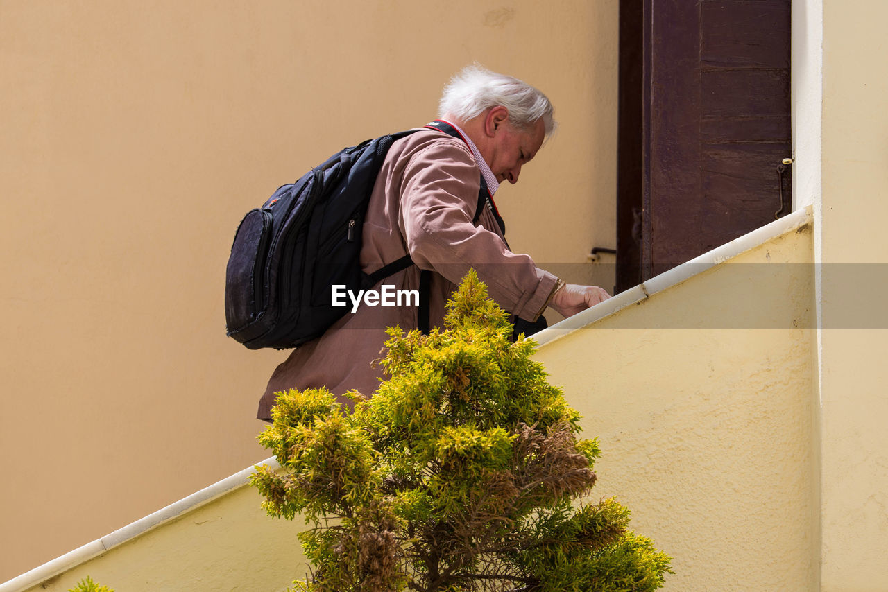 MAN STANDING BY PLANTS AGAINST WALL