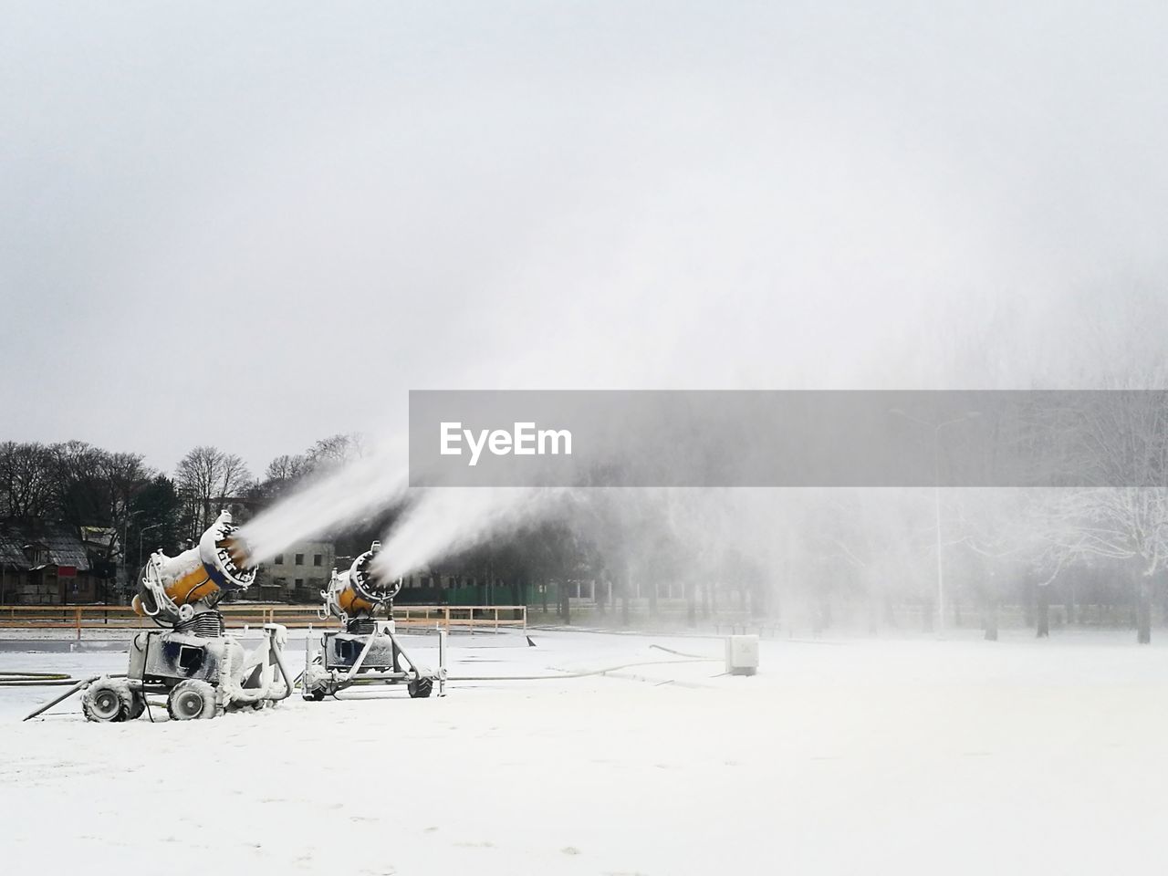 Two yellow snow blowers working on snow for cross country skiing slope in the city park at daylight