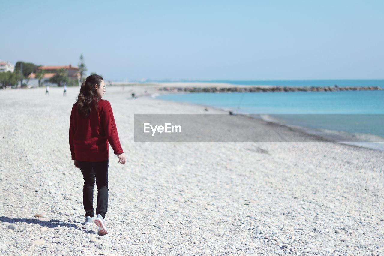 Rear view of woman on beach against clear sky