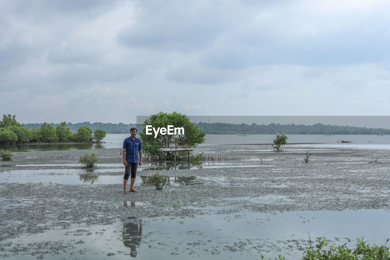 water, sky, cloud, shore, nature, full length, beach, men, land, day, sea, one person, plant, beauty in nature, body of water, lifestyles, adult, leisure activity, casual clothing, childhood, scenics - nature, child, outdoors, wet, tree, walking, rear view, tranquility, standing, non-urban scene, environment, occupation, wetland, coast, holiday, sand, reflection