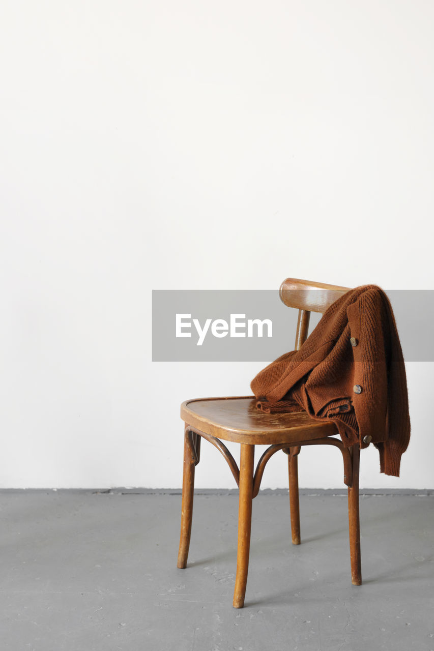 A knitted jacket made of brown woolen yarn lies on a wooden chair.