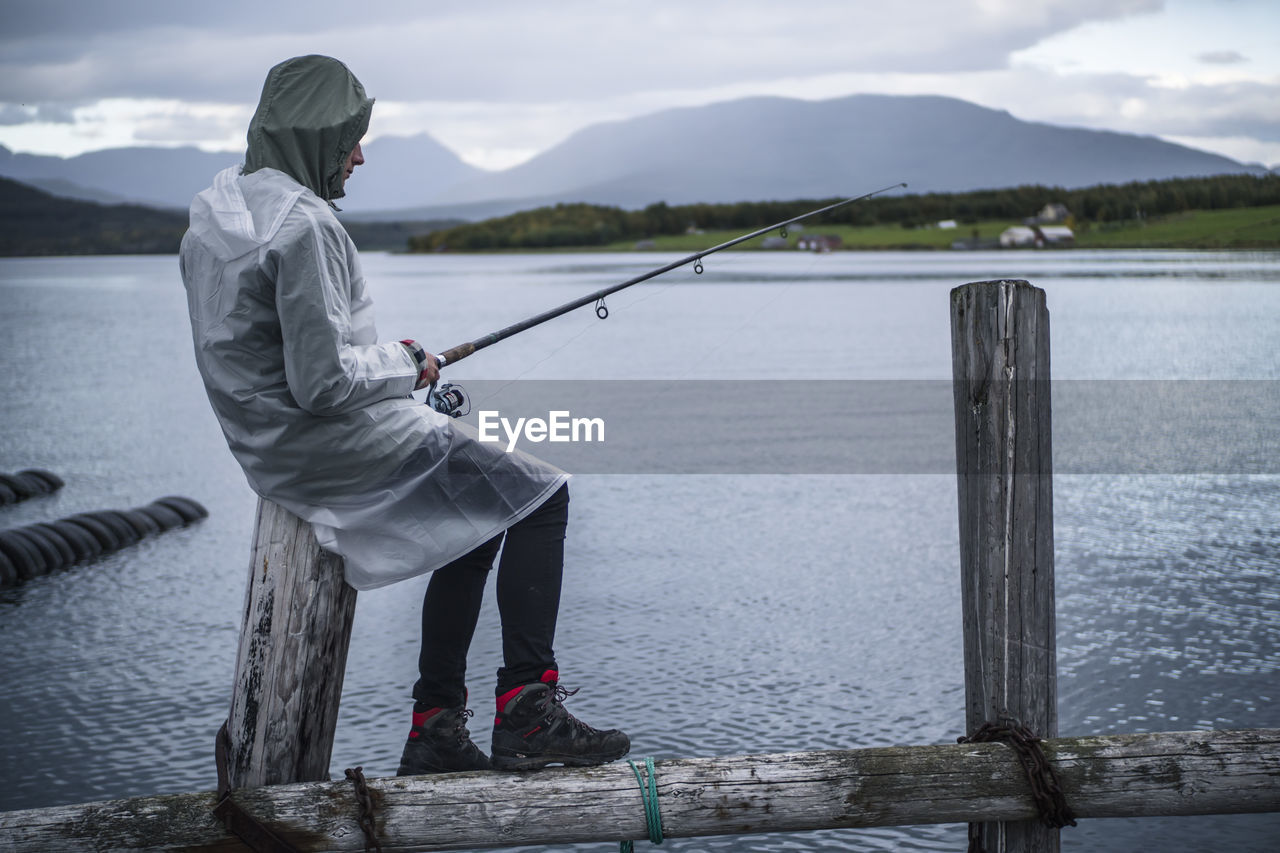 Man fishing in river against mountains