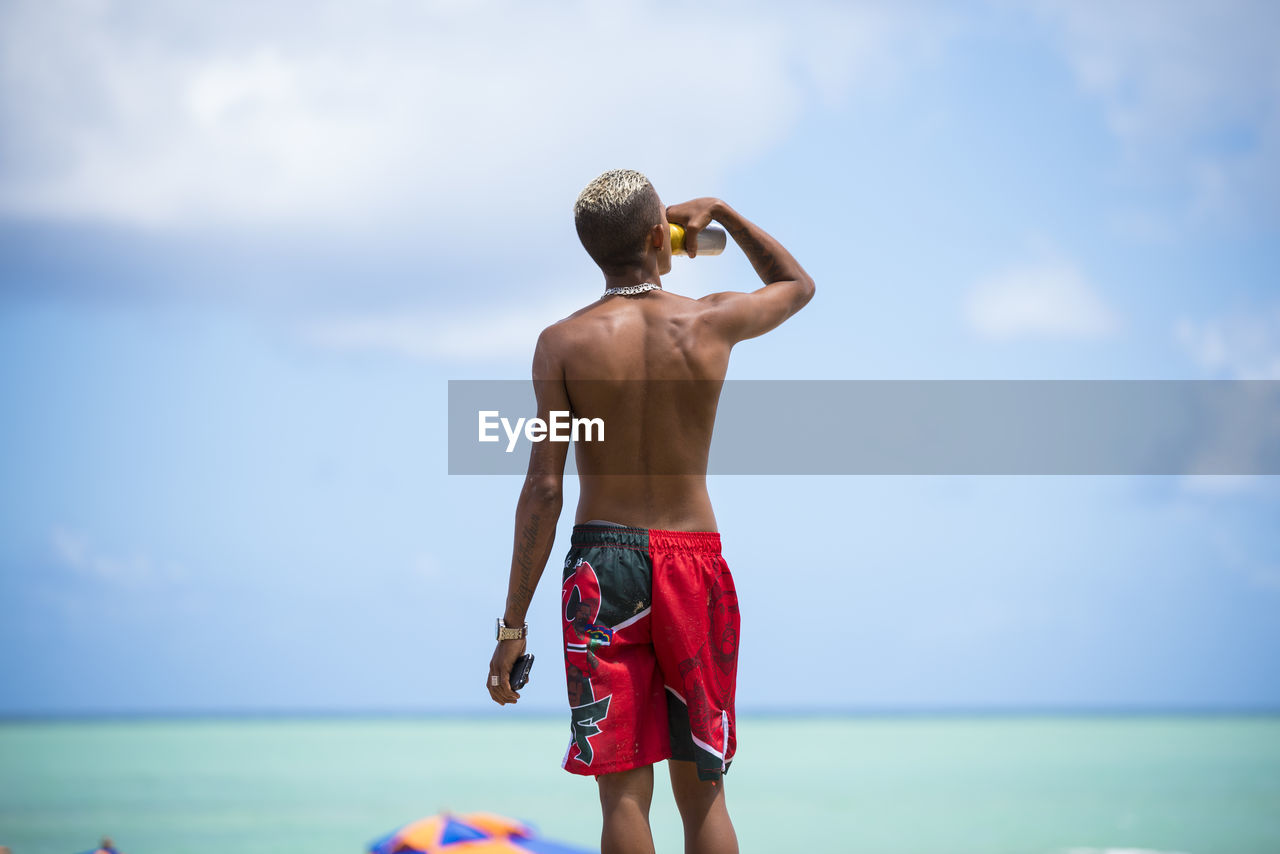 REAR VIEW OF MAN LOOKING AT SEA