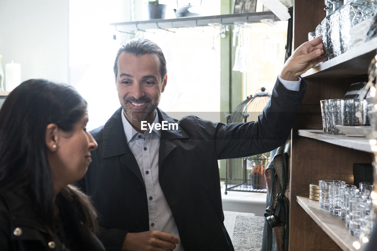 Smiling mature customers talking while standing by rack with glassware at store