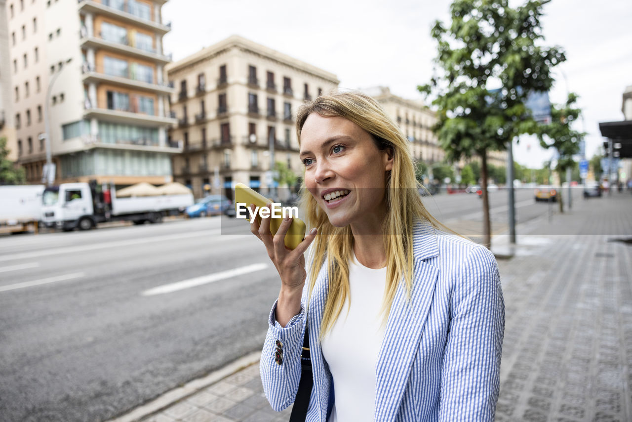 Contemplative businesswoman talking on speaker phone at sidewalk