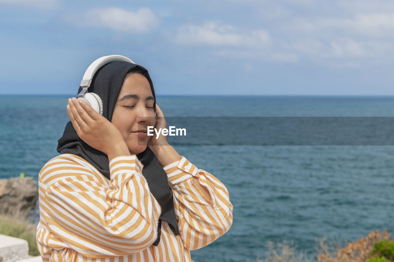 Smiling maghrebi woman with hijab listening to music