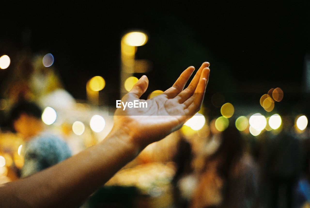 Close-up of woman hand against illuminated lights at night