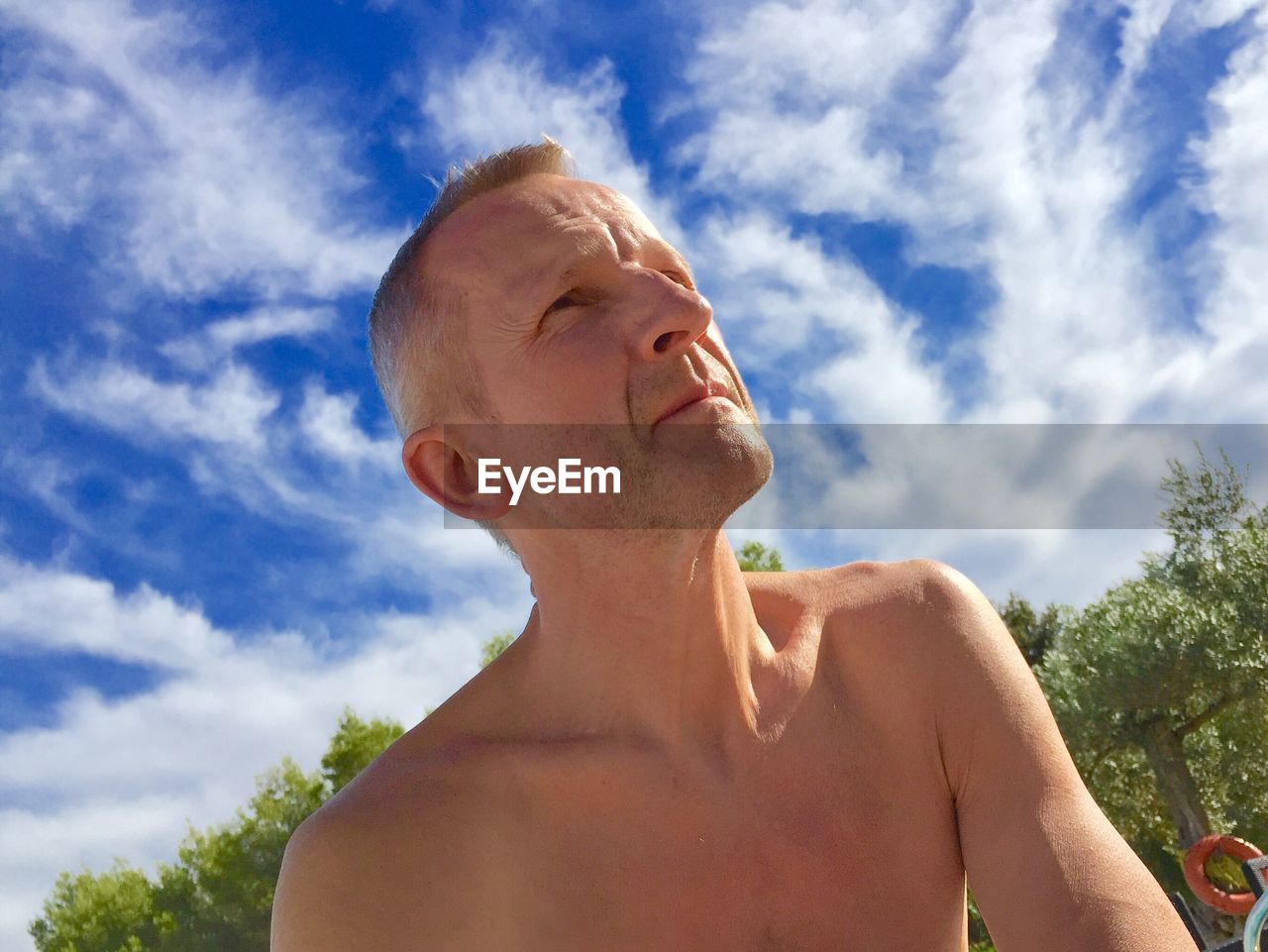 Low angle view of shirtless mature man against sky