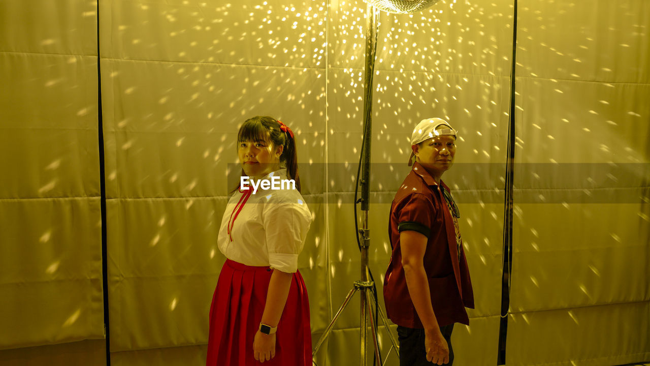 Man and woman standing by curtain with disco ball reflection