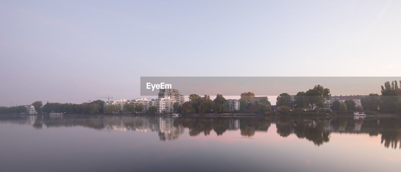 REFLECTION OF TREES AND BUILDINGS IN LAKE AGAINST SKY