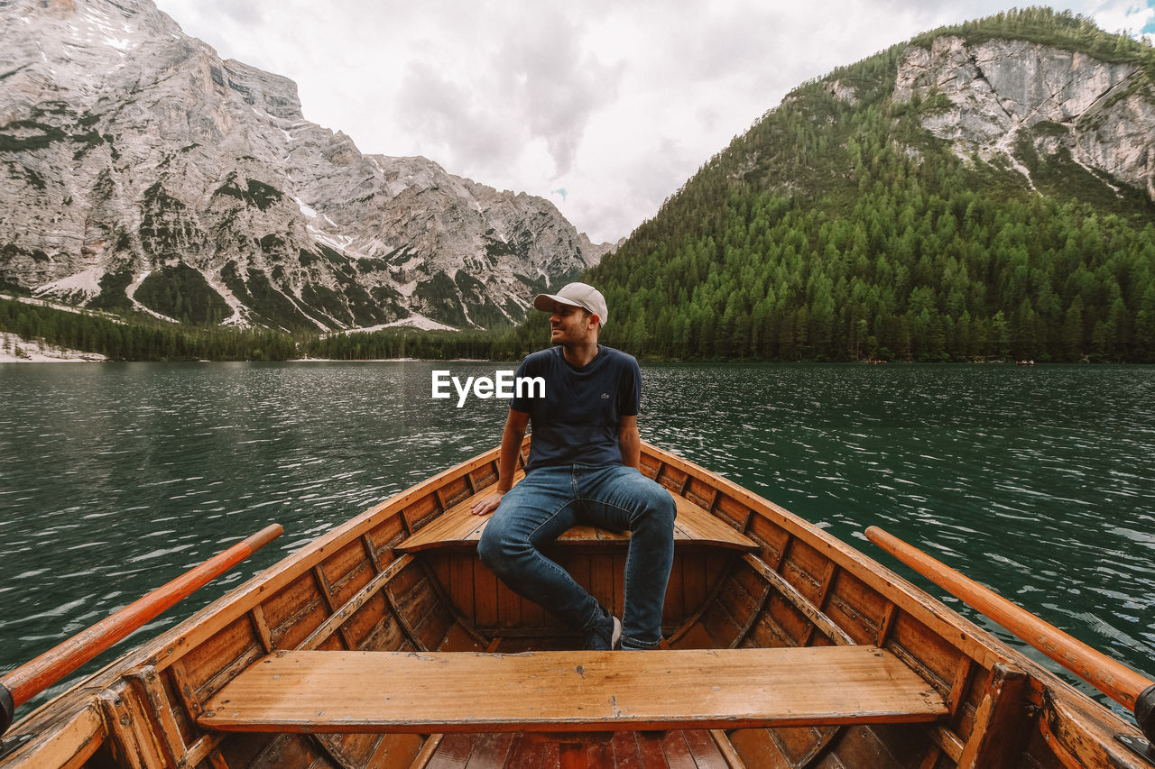 MAN SITTING ON LAKE AGAINST MOUNTAIN